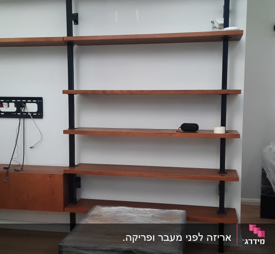 מדפים מעץ ומתכת על קיר לבן, שולחן עטוף בניילון
